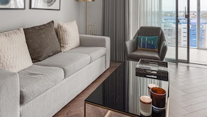 A modern living room with a grey sofa, a glass coffee table, and a city view through large windows. - Battersea Power Station Flat With River Views (London)