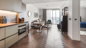 A modern apartment with a kitchen, dining area, and a living room with a large window. - Battersea Power Station Flat With River Views (London)