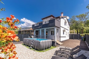 Ein zweistöckiges Haus mit Swimmingpool, Sitzgelegenheiten im Freien und einem Garten.