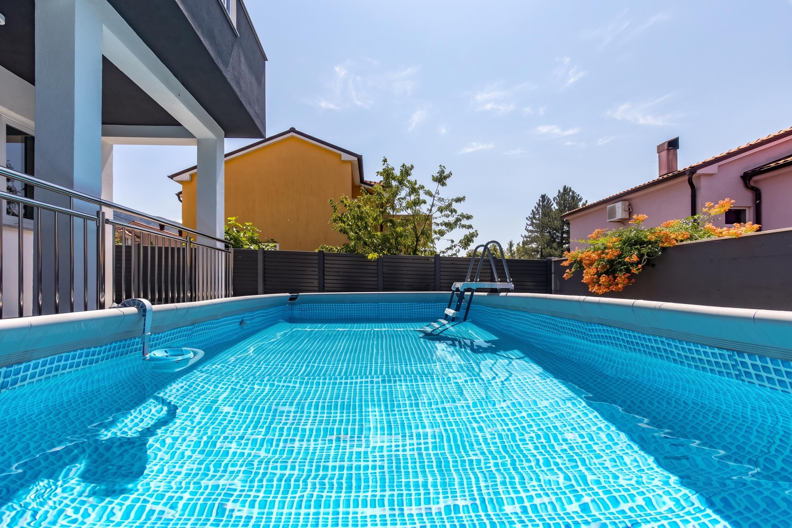 A swimming pool with a tiled floor, surrounded by a fence, and adjacent to buildings.