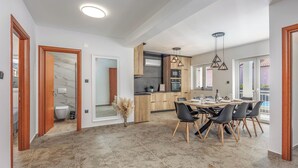 A modern kitchen with wooden cabinets, a dining area with a table and chairs, and a large window providing natural light. - Pool House Beba Tribalj Lake (Vinodol)
