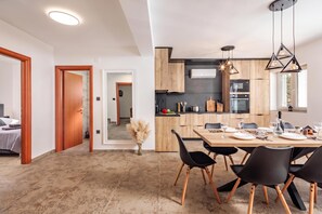 Une cuisine moderne avec des meubles en bois, un coin repas avec une table dressée pour deux personnes, et un couloir menant à une chambre.