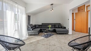 A modern living room with a sectional sofa, two black chairs, a small table with a vase, and a wooden door. - Pool House Beba Tribalj Lake (Vinodol)