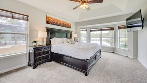 A bedroom with a dark wooden bed, a ceiling fan, a large window, and a TV mounted on the wall. - Private Patio + Lake View: Fruit Cove Home (St. Johns)