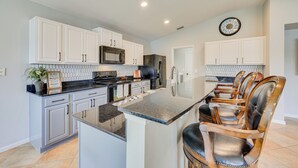 A modern kitchen with white cabinets, stainless steel appliances, and a central island with bar stools. - Private Patio + Lake View: Fruit Cove Home (St. Johns)