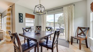 A dining area with a wooden table and chairs, a modern chandelier, and a view of the outdoors through large windows. - Private Patio + Lake View: Fruit Cove Home (St. Johns)