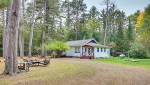 Une cabane dotée d’un porche, entourée de grands arbres et bordée d’une pelouse.