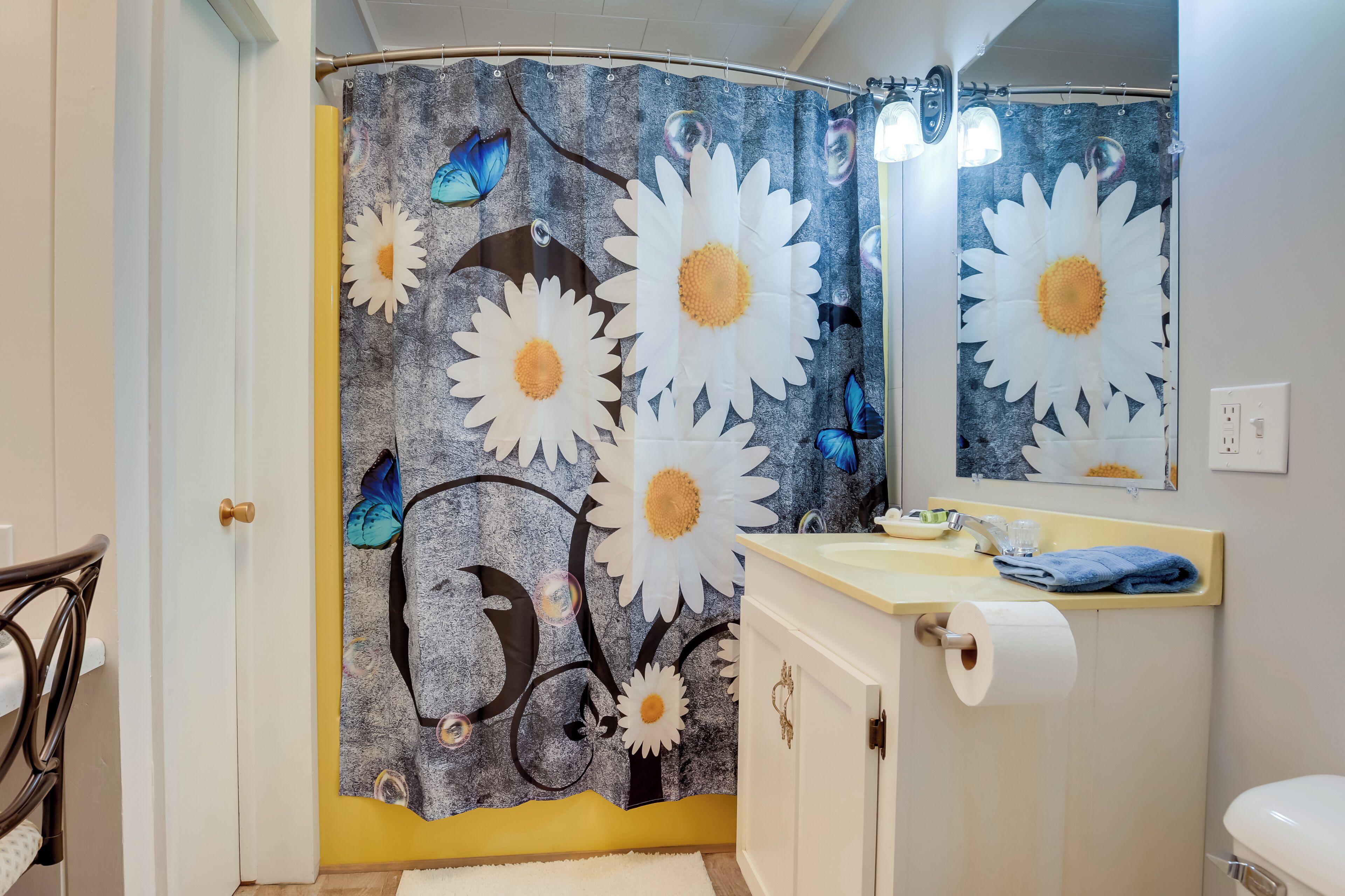 A bathroom with a shower curtain featuring floral and butterfly designs, a sink with a towel, and a toilet.