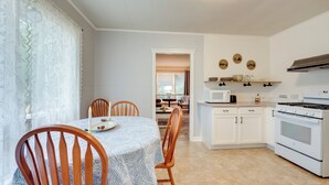 Une cuisine avec des meubles blancs, une cuisinière et un four à micro-ondes. On y trouve une table à manger avec des chaises et une nappe blanche.