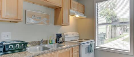 A kitchen with wooden cabinets, a granite countertop, a white stove, and a window with blinds.