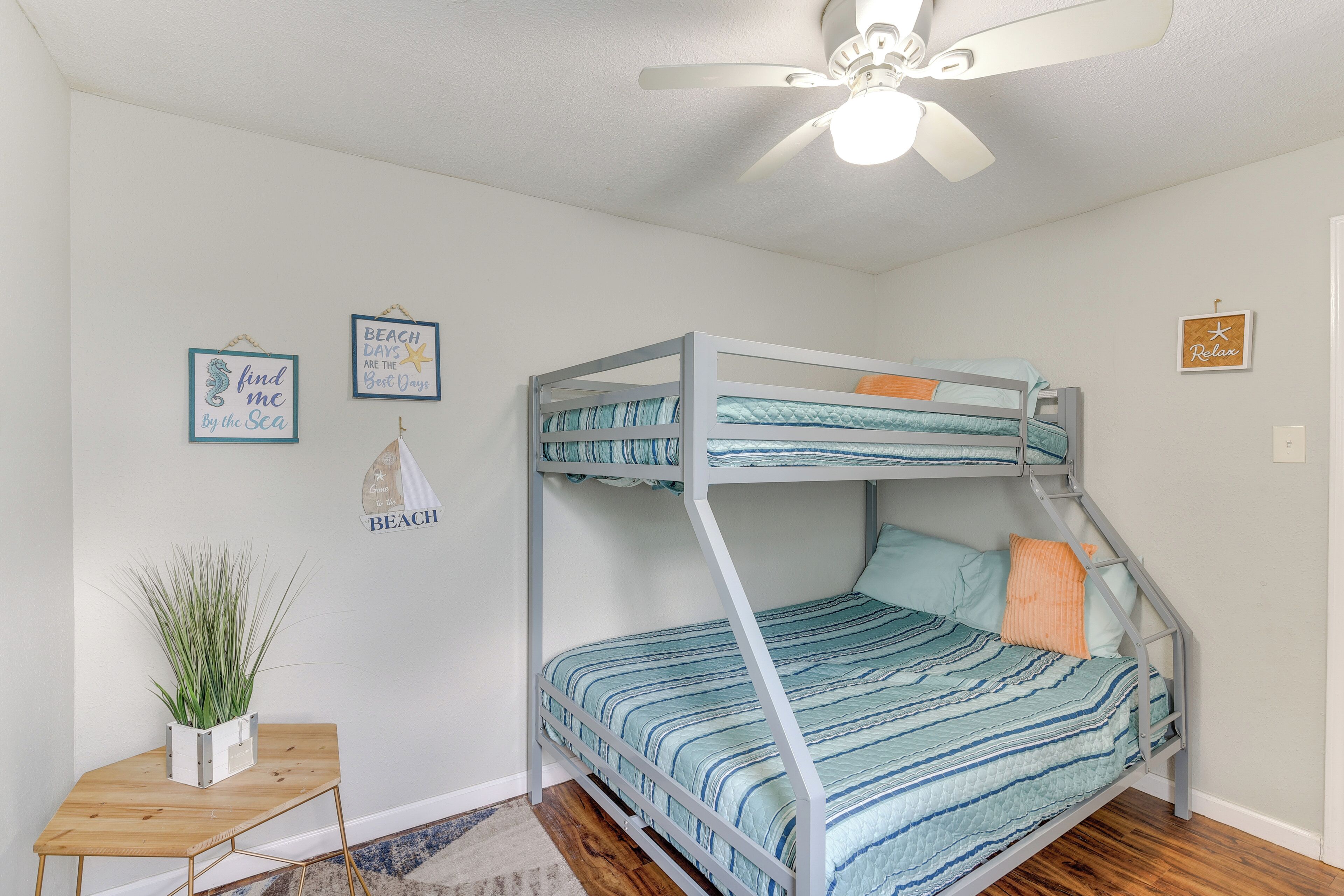 A bunk bed room with a ceiling fan, a small table with a plant, and wall decorations including a 'Beach Days' sign.