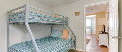 Una cama litera con ropa de cama a rayas, un ventilador de techo y un pasillo que conduce a una zona de cocina.