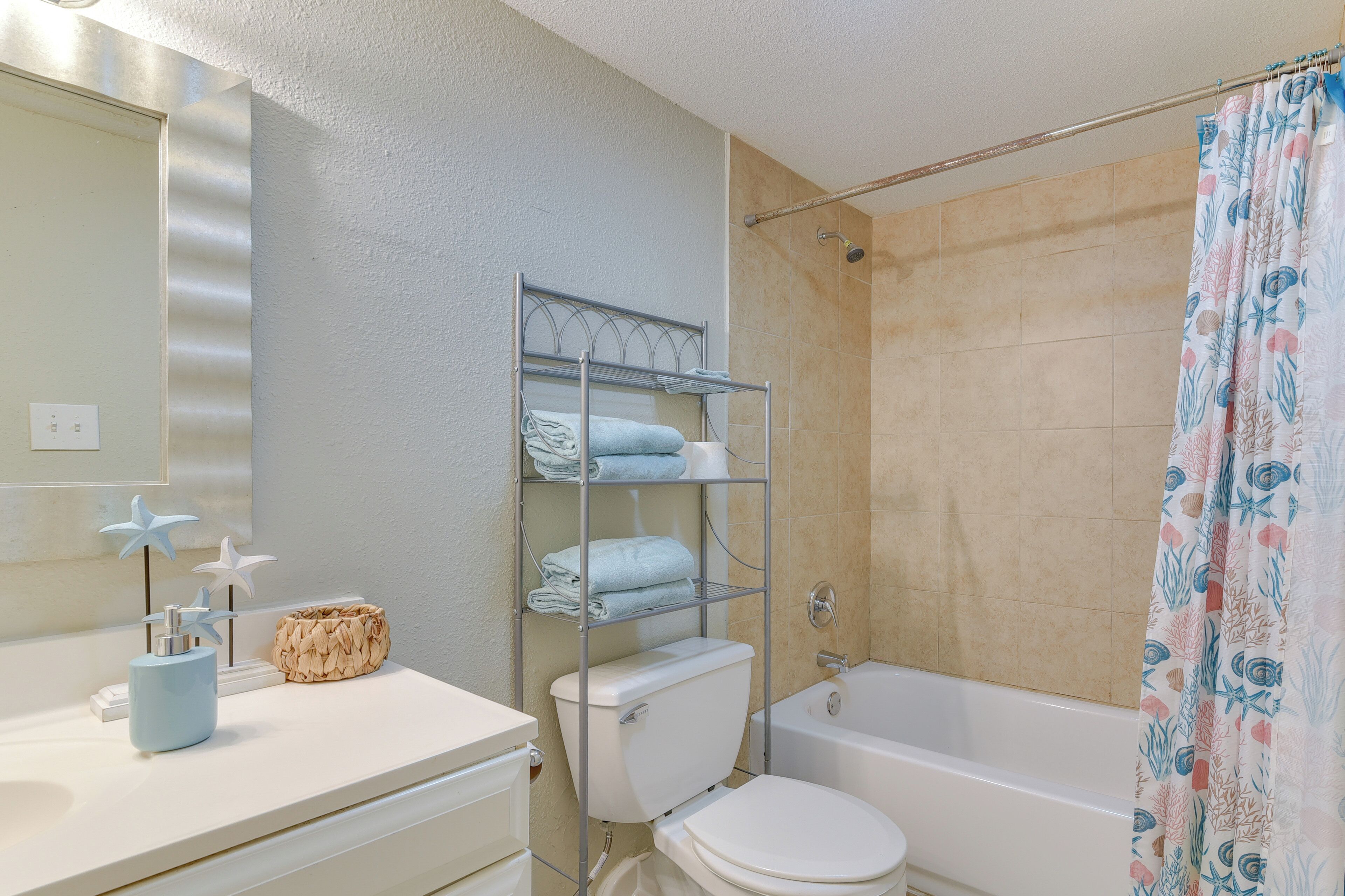 Een badkamer met toilet, bad, douchegordijn, plank met handdoeken en spiegel.