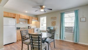 A kitchen with wooden cabinets, a refrigerator, a ceiling fan, and a dining table with chairs.