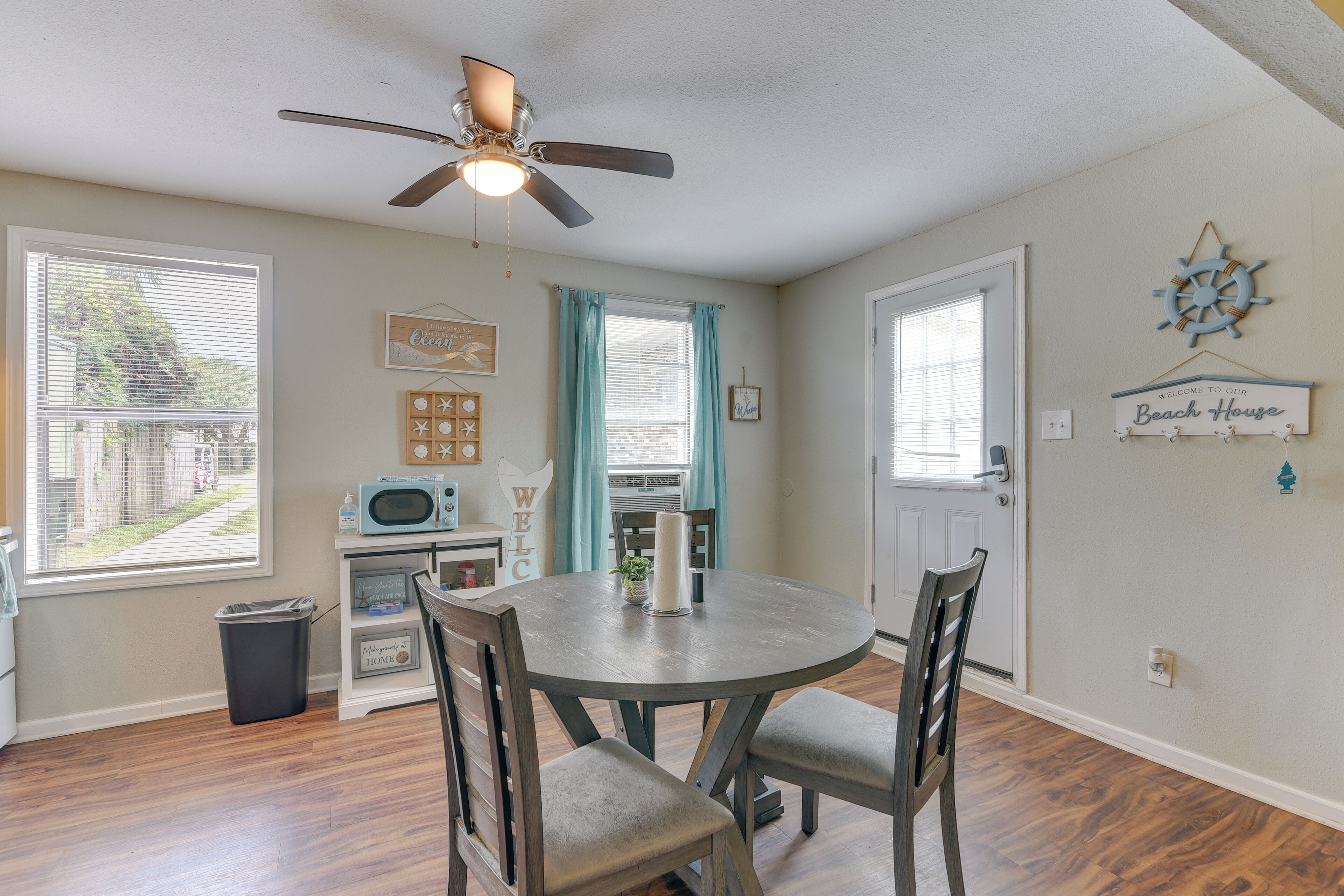A dining area with a round table, chairs, a ceiling fan, and a view of the outdoors.
