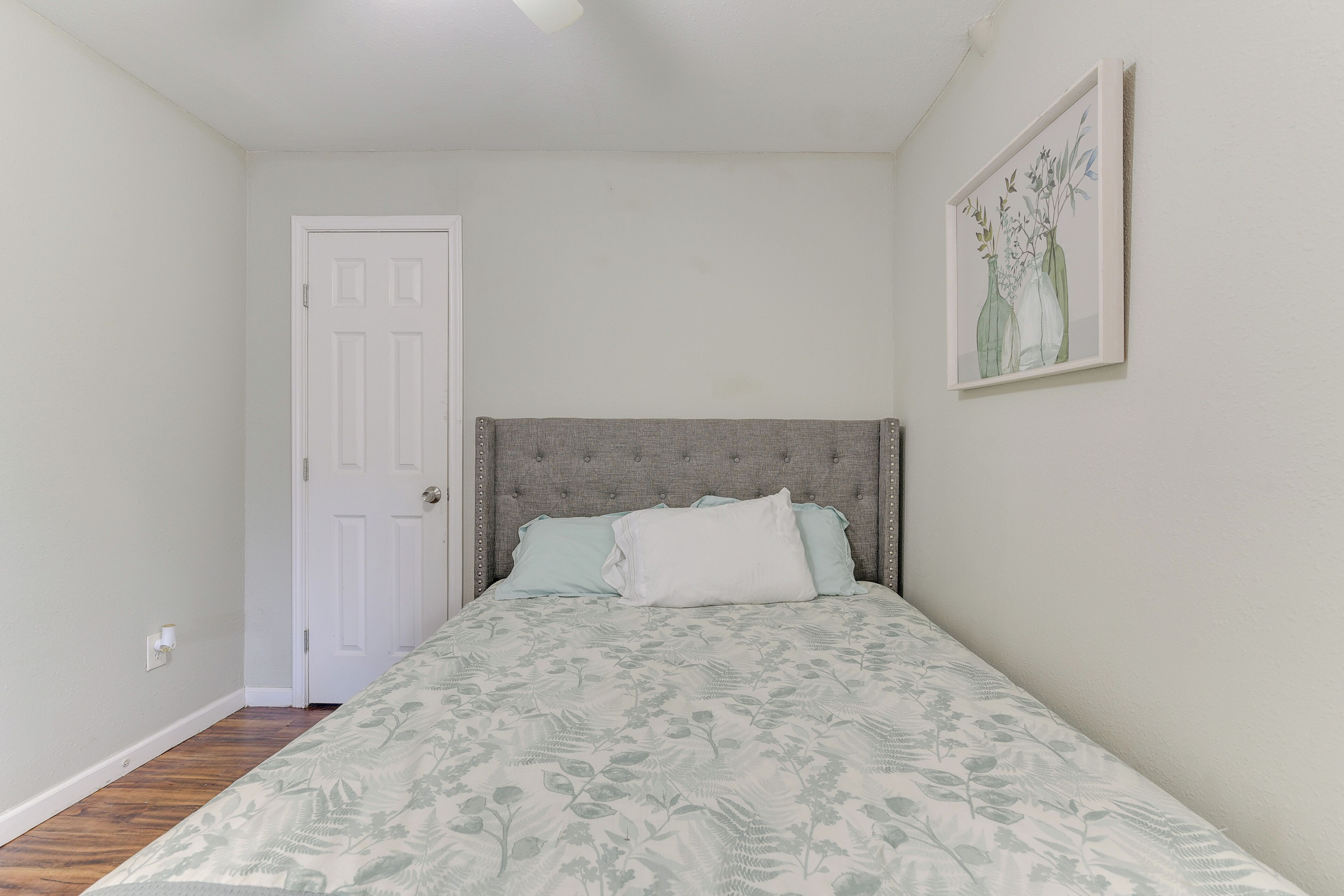 A bedroom with a bed, a door, and a framed picture on the wall.