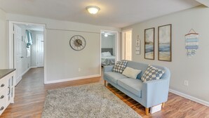 A living room with a light blue sofa, a gray rug, and a wall clock. There are framed pictures on the wall and a hanging sign.
