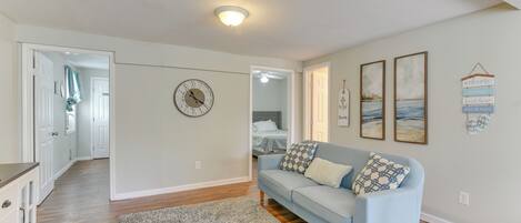 A living room with a light blue sofa, a gray rug, and a wall clock. There are framed pictures on the wall and a hanging sign.