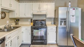 Una cocina con armarios blancos, una estufa de acero inoxidable, un refrigerador y un reloj en la pared.