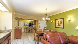 A spacious living room with a leather sofa, a dining area with a wooden table and chairs, and a kitchen in the background.