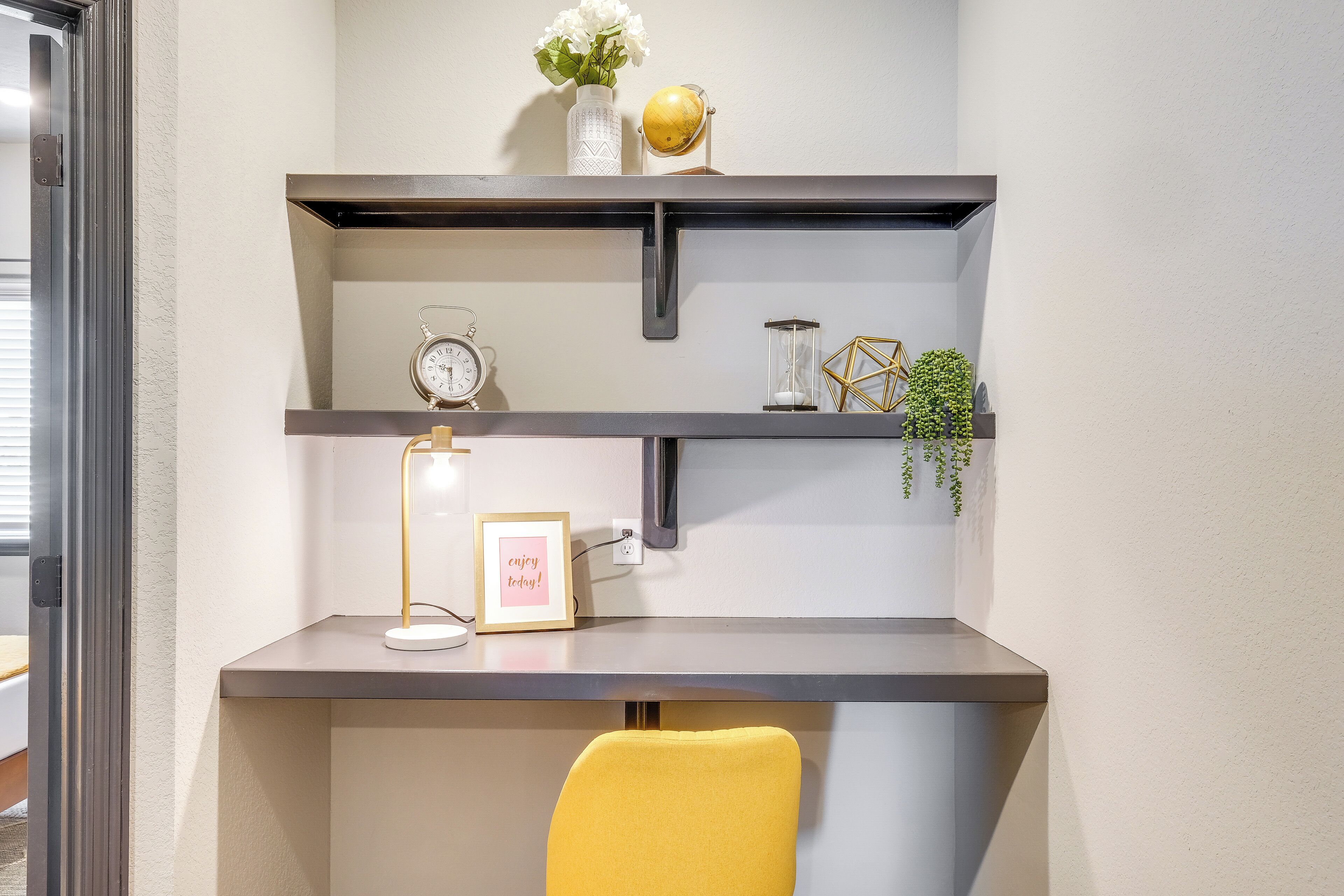 Un escritorio con estantes superiores, un reloj, un cuadro enmarco y una silla amarilla.