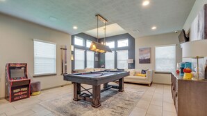 Un salon spacieux comprenant une table de billard, une lampe de table de billard, un canapé et une machine à café.