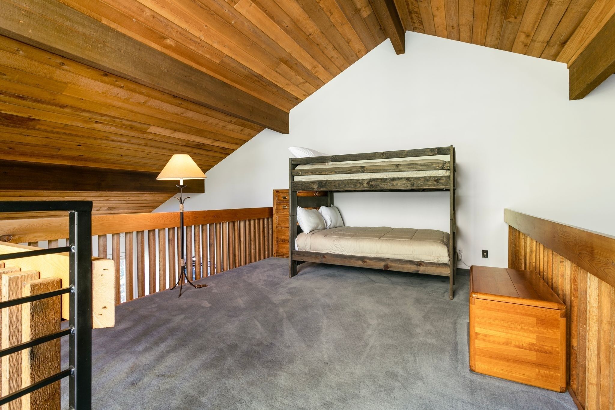 A loft bedroom with a bunk bed, a lamp, and a wooden chest of drawers.