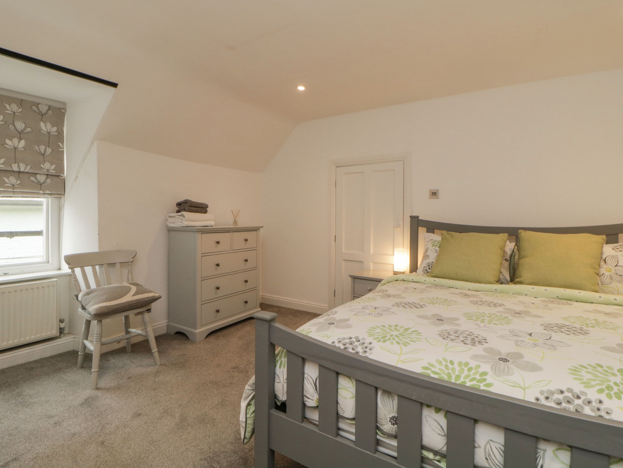 Une chambre à coucher avec un lit, une commode, une chaise et une fenêtre avec des rideaux.