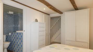 A bedroom with a bed, a wardrobe, a chest of drawers, a staircase, and a bathroom with a toilet and blue-tiled walls.