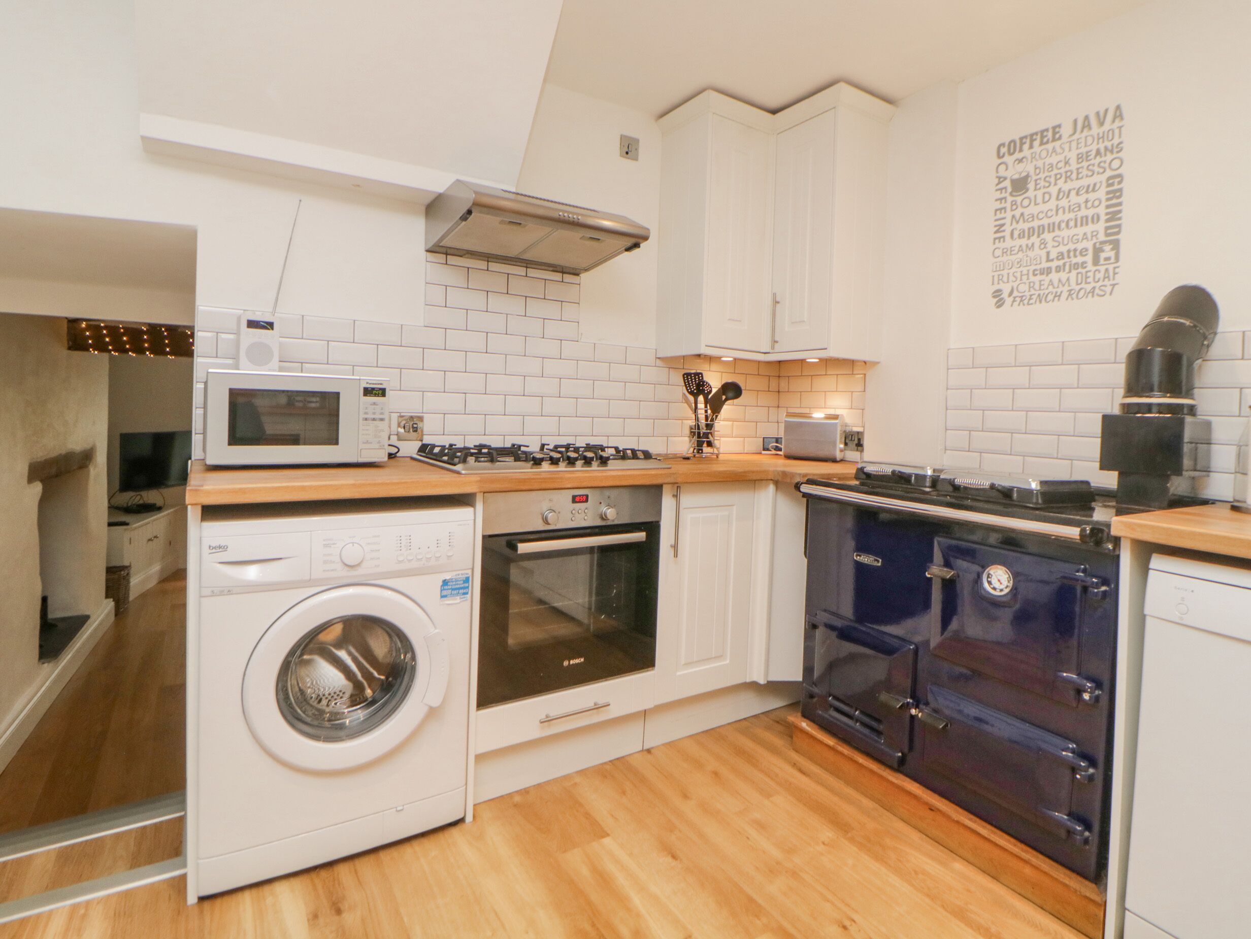 A compact kitchen with a washing machine, oven, stove, and a coffee machine.