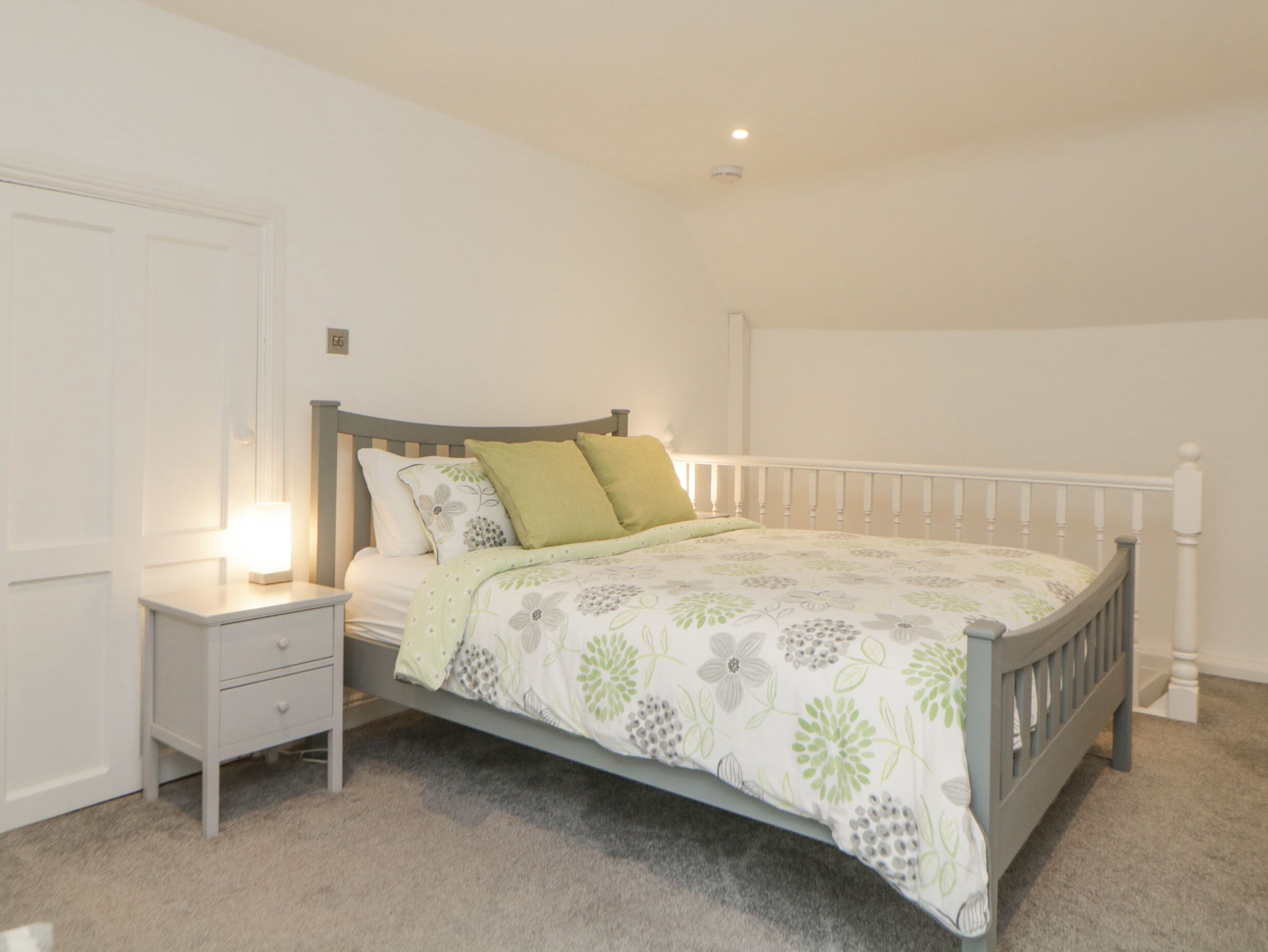 A bedroom with a bed, nightstand, and a wall-mounted light.