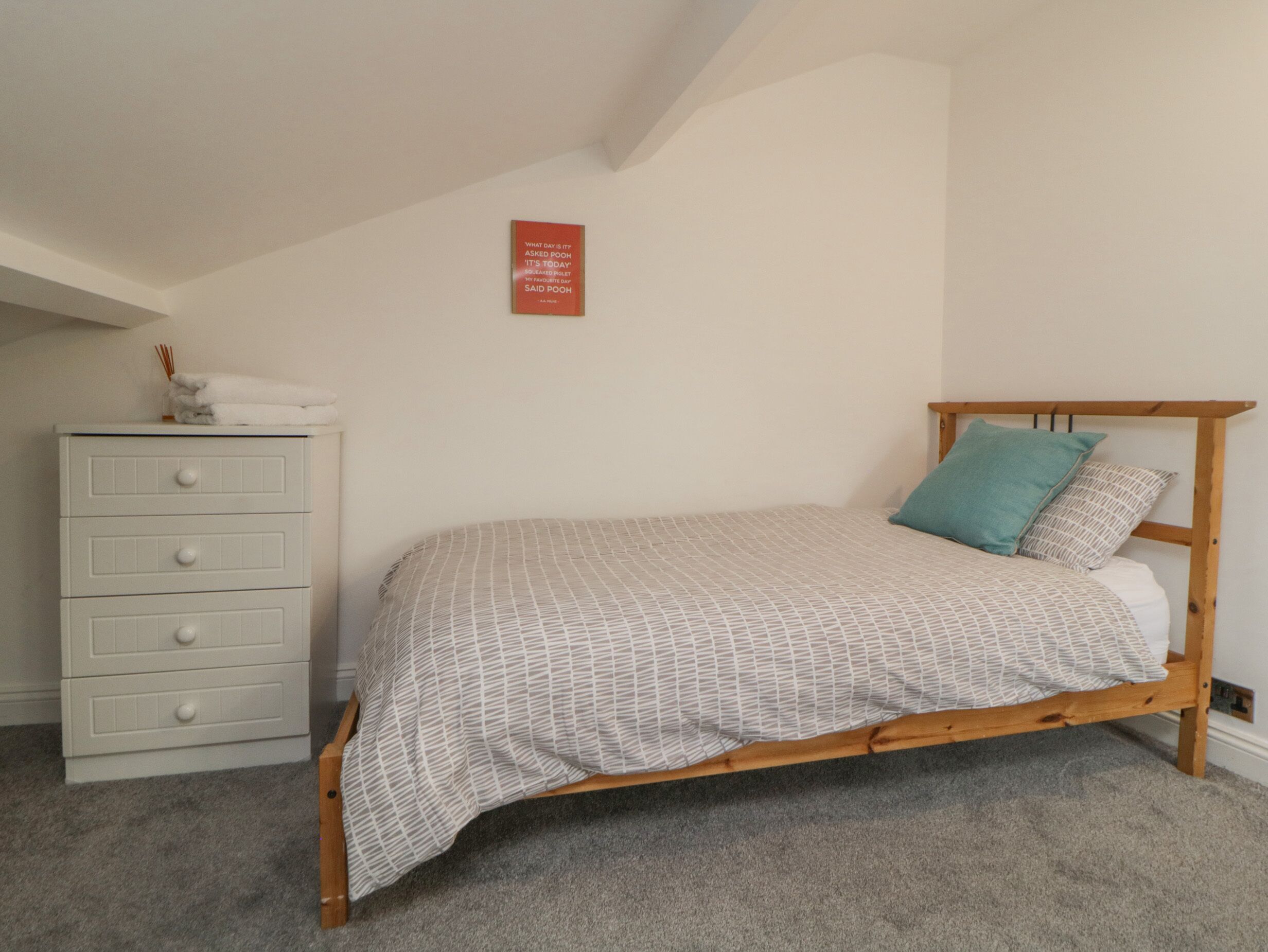 Un dormitorio con una cama de madera, un aparador blanco y un letrero en la pared.
