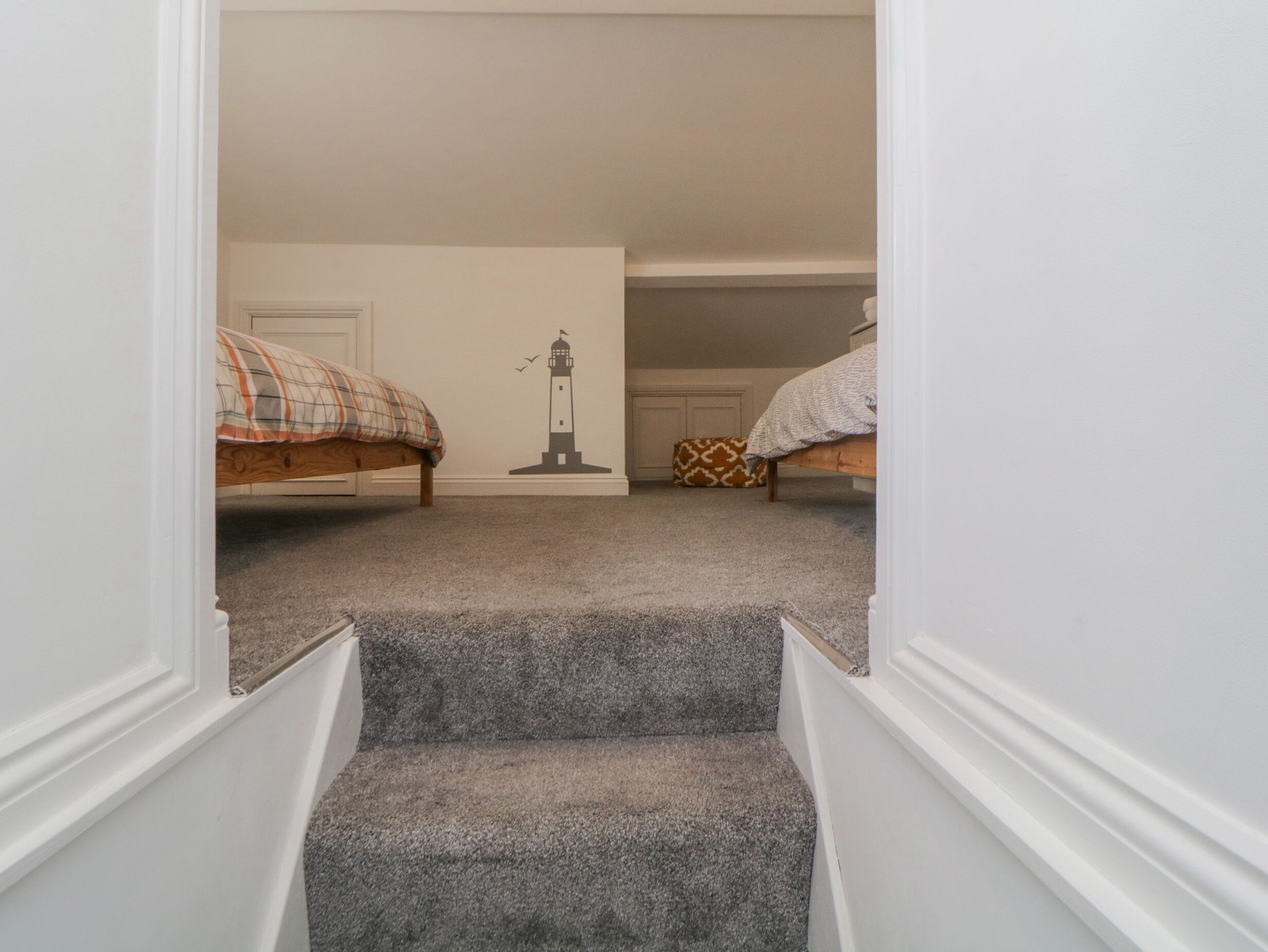 A narrow hallway with carpeted stairs leading to two bedrooms, each with a bed and a nightstand.
