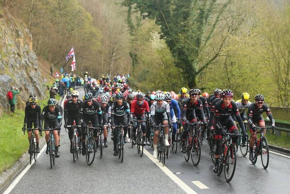 A group of cyclists on a road with a flag on the left.