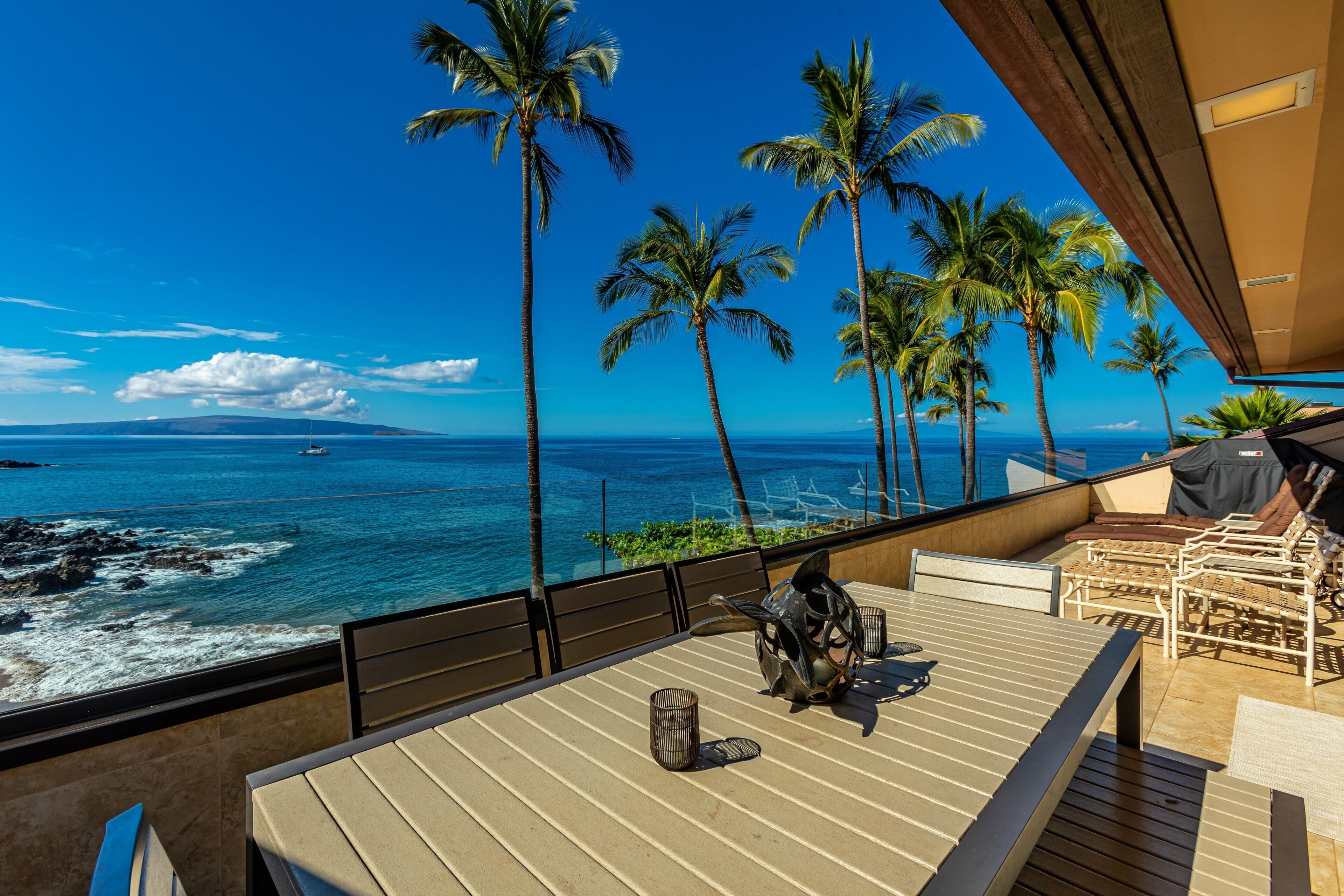 Terraço com vista para o oceano e palmeiras, com área de estar ao ar livre e uma escultura decorativa.