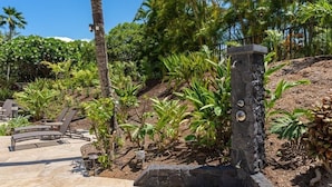 A landscaped outdoor area with a curved seating arrangement, a stone pillar, and various tropical plants.