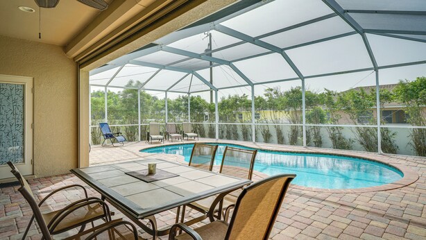 A covered outdoor area with a pool, patio furniture, and a table. - Lanai + Pool: Family-friendly Home in Cape Coral (Cape Coral)