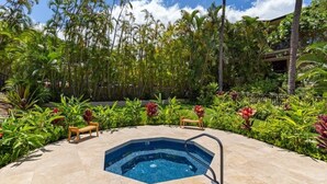 Een jacuzzi omringd door weelderige tropische beplanting en een houten bank.
