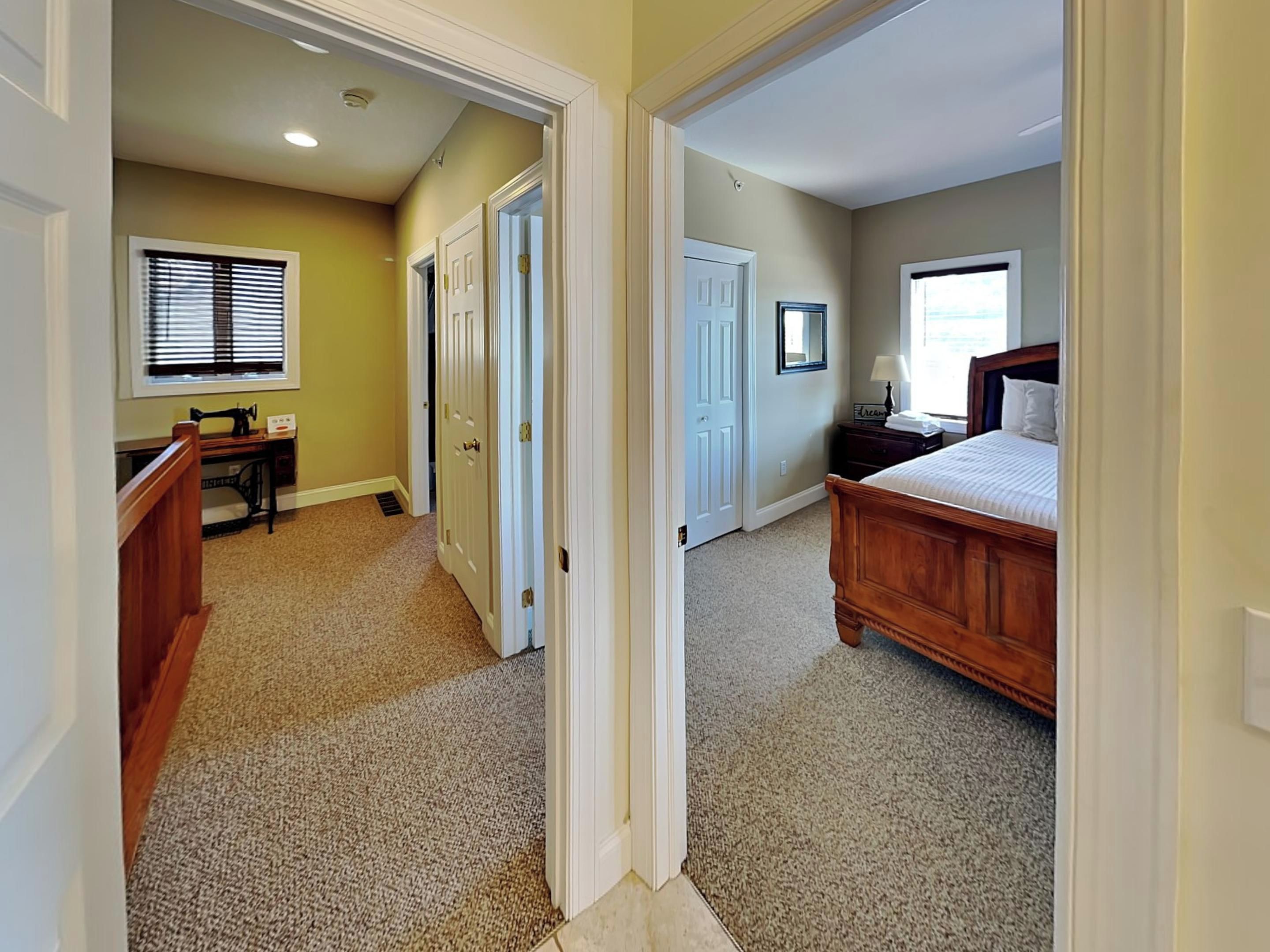 A bedroom with a bed, a desk, and a chair, carpeted floors, and a window with blinds.