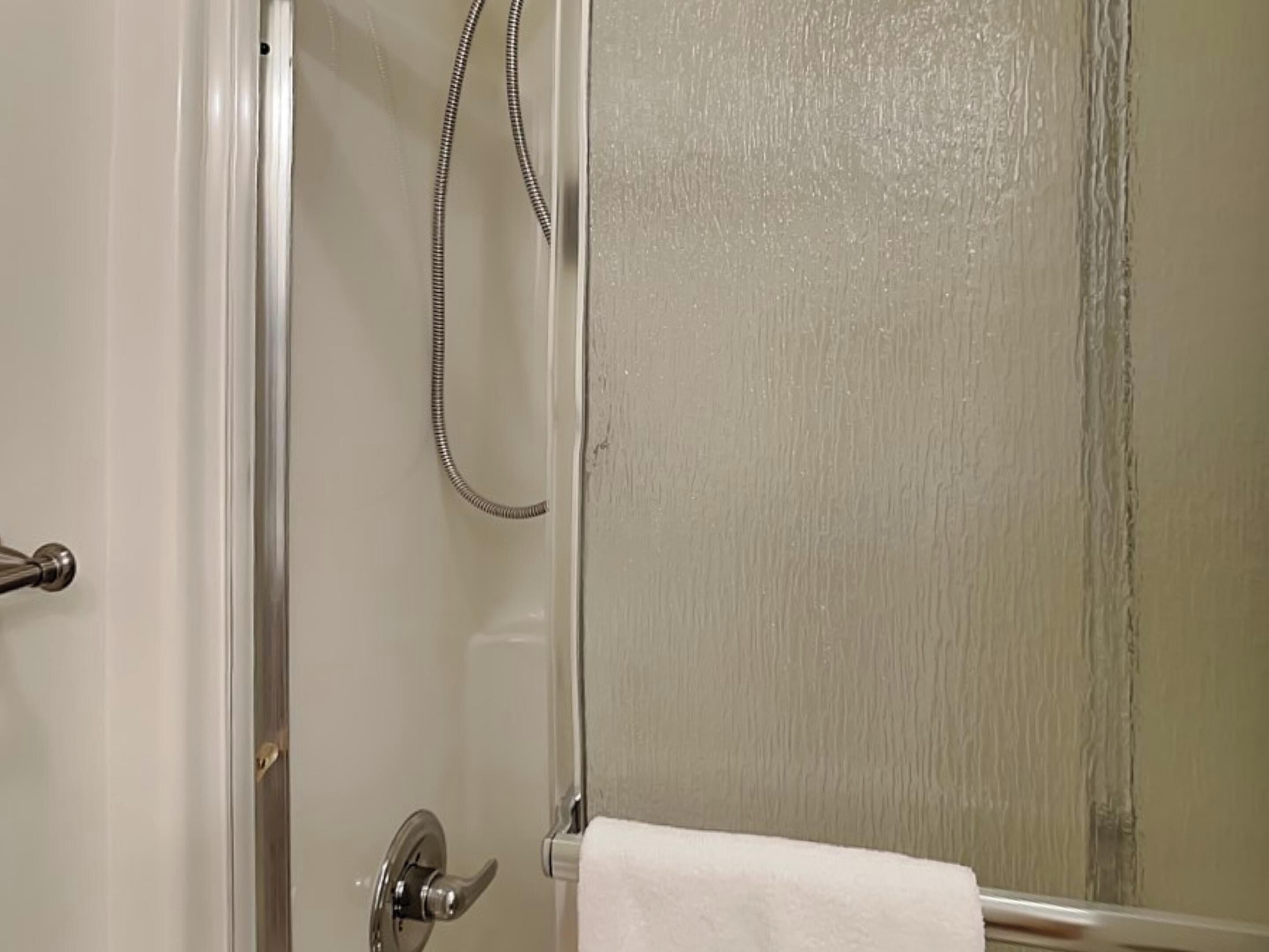 Una ducha con puerta de vidrio y un cabezal de ducha manual.