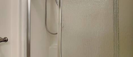 Una ducha con puerta de vidrio y un cabezal de ducha manual.