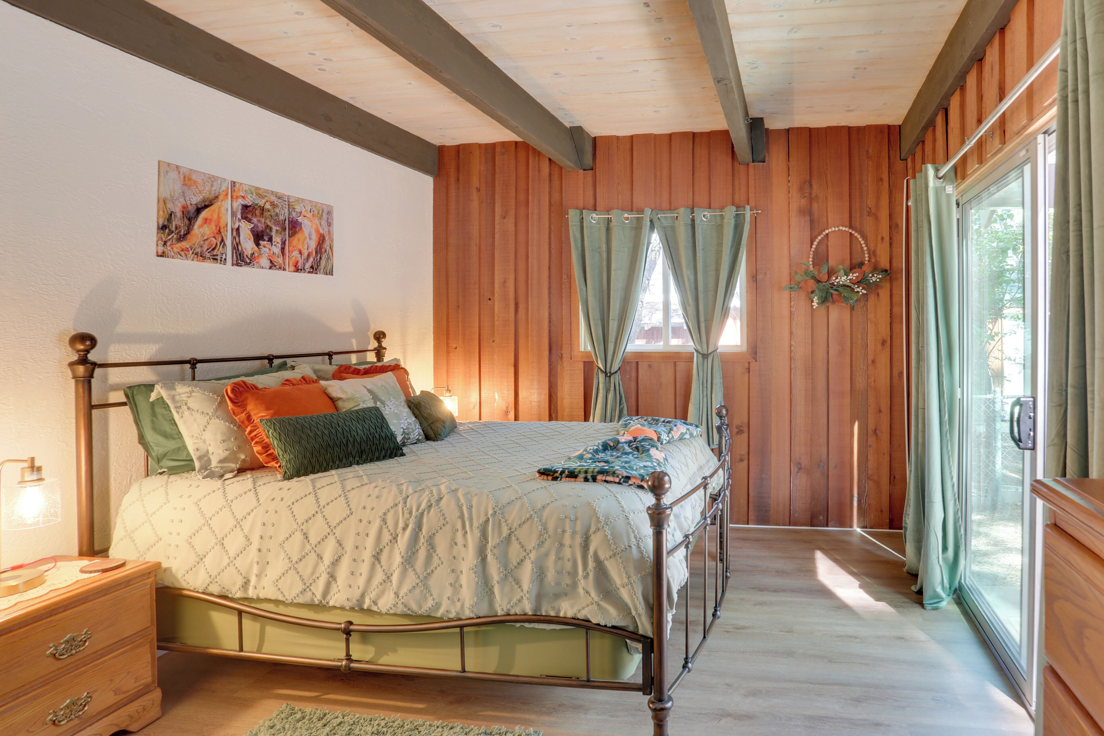 Una camera da letto con soffitto in legno, un letto con copriletto trapuntato, un comodino, una finestra con tende e un'opera d'arte appesa al muro.