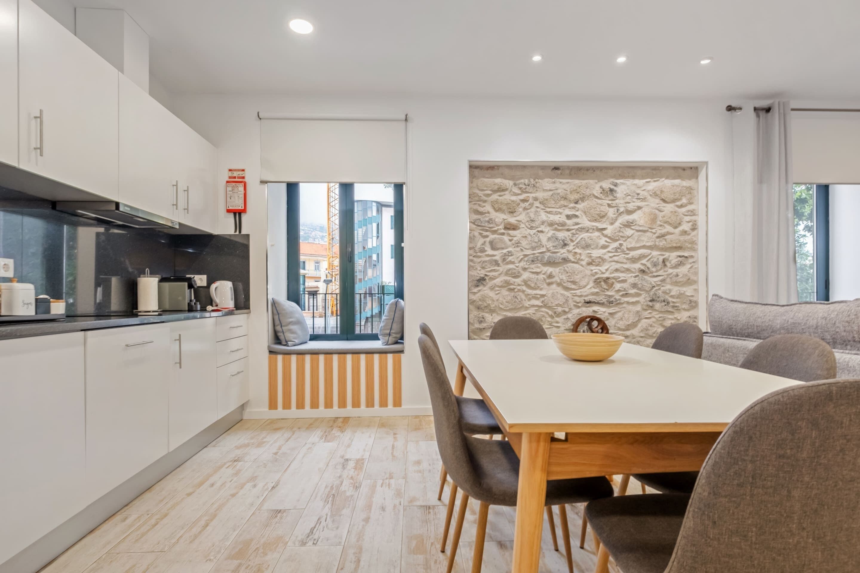 A modern kitchen with white cabinets, a stone accent wall, and a dining area with a wooden table and chairs.