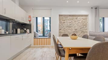 A modern kitchen with white cabinets, a stone accent wall, and a dining area with a wooden table and chairs.