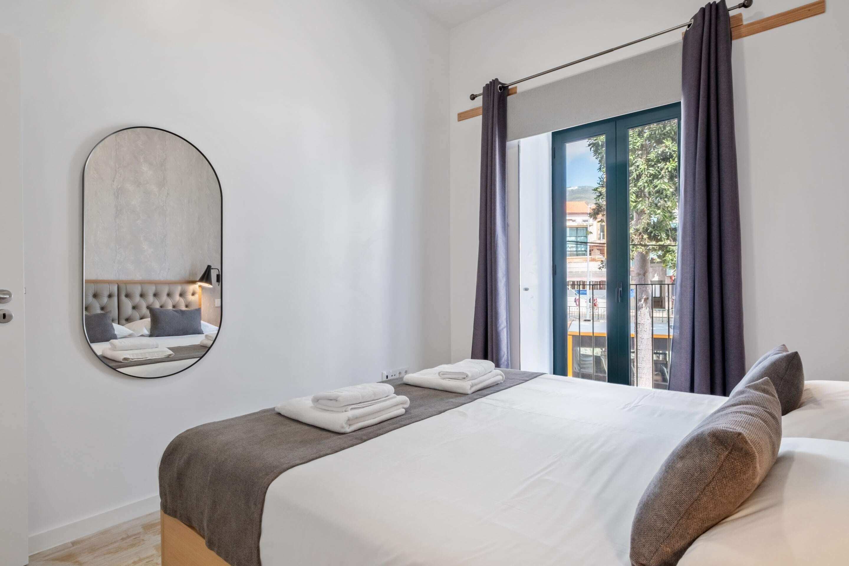 Ein modernes Hotelzimmer mit einem Bett, einem großen Spiegel und Blick nach draußen durch eine Schiebetür.