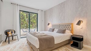A modern bedroom with a large bed, a chair, a small table, and a view of the outdoors through a sliding door. - Tanoeiros Residence by An Island Apart (Funchal)