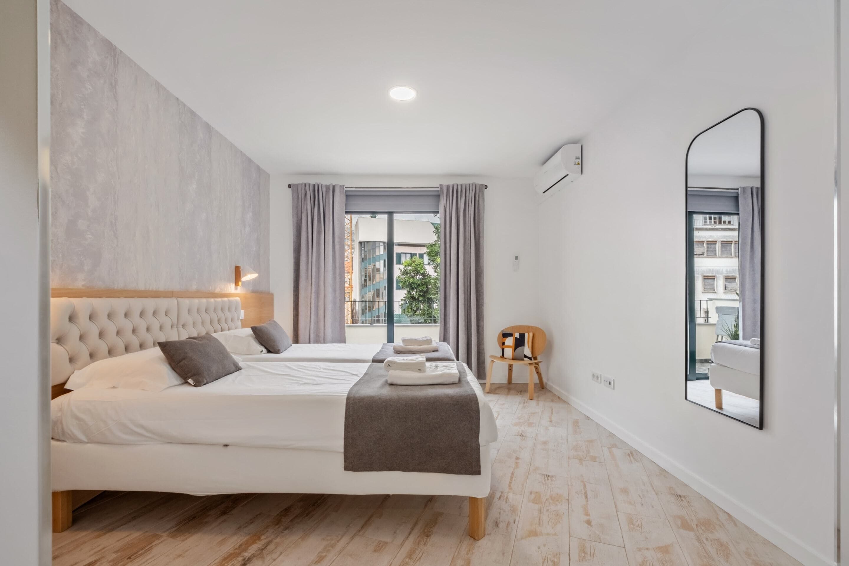 A modern bedroom with a large bed, a smaller bed, a mirror, and a view of the outside.