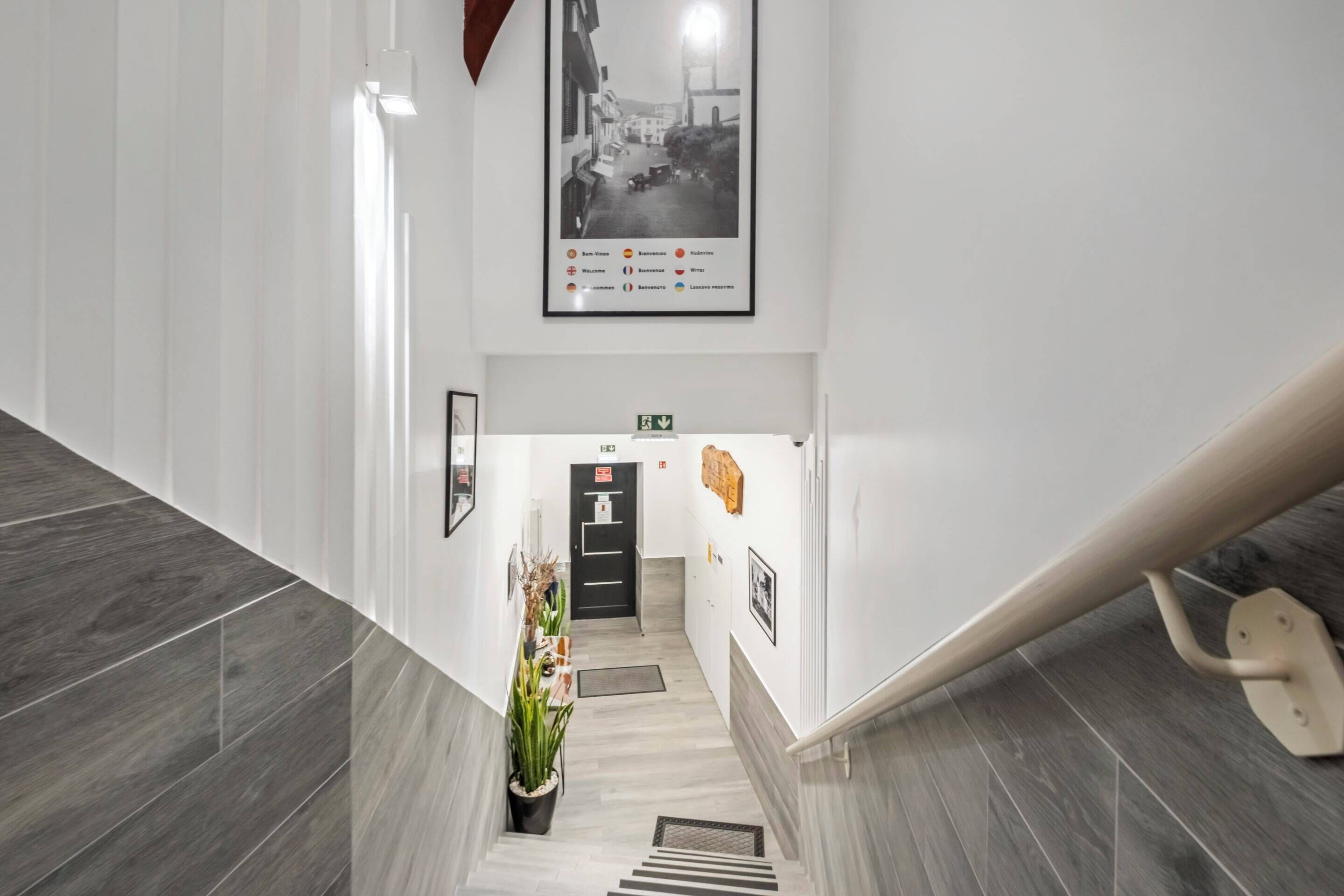 A modern hotel lobby with a staircase, a black door, and a framed photo on the wall.
