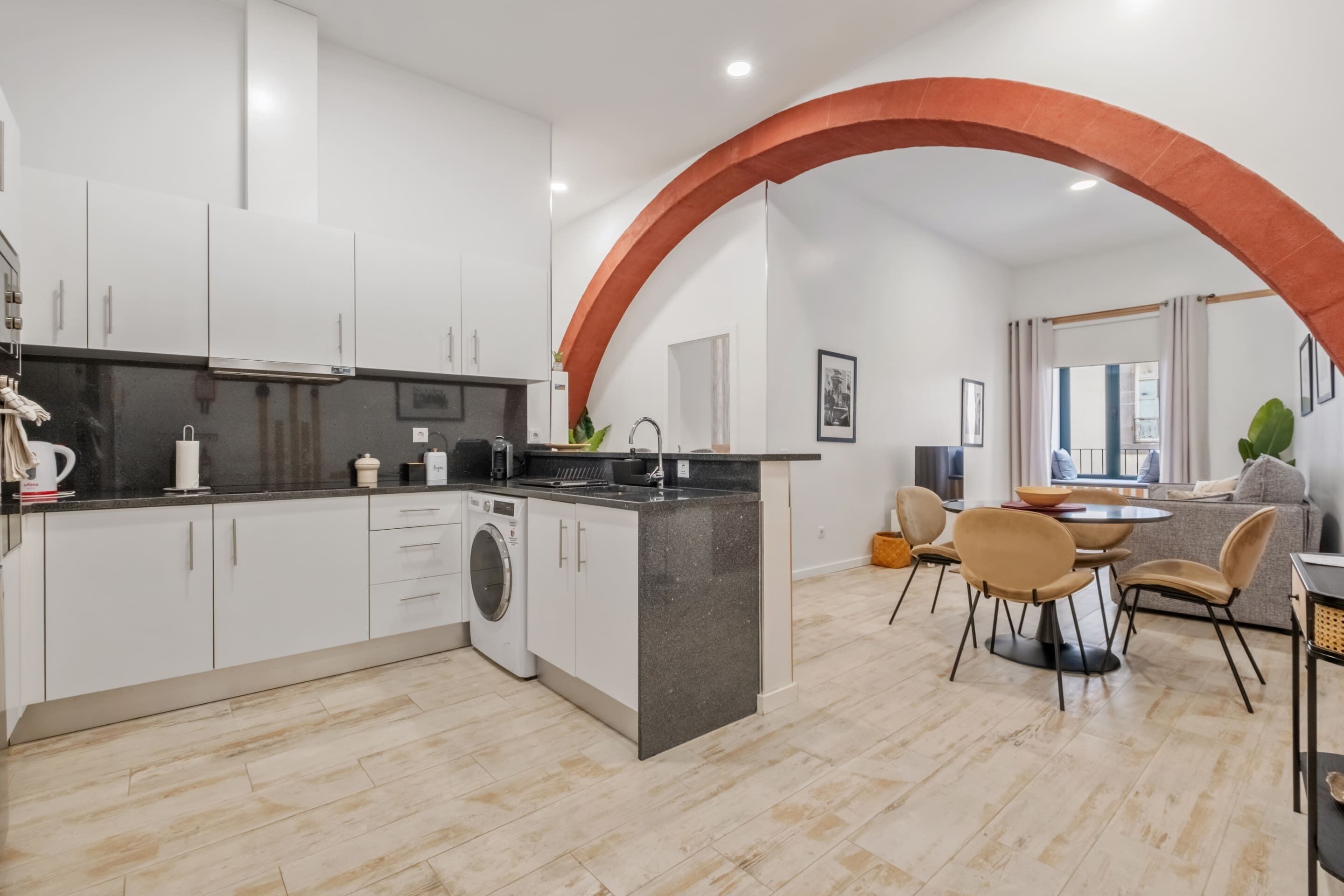 A modern kitchen with white cabinets, a washing machine, and a dining area with a round table and chairs.