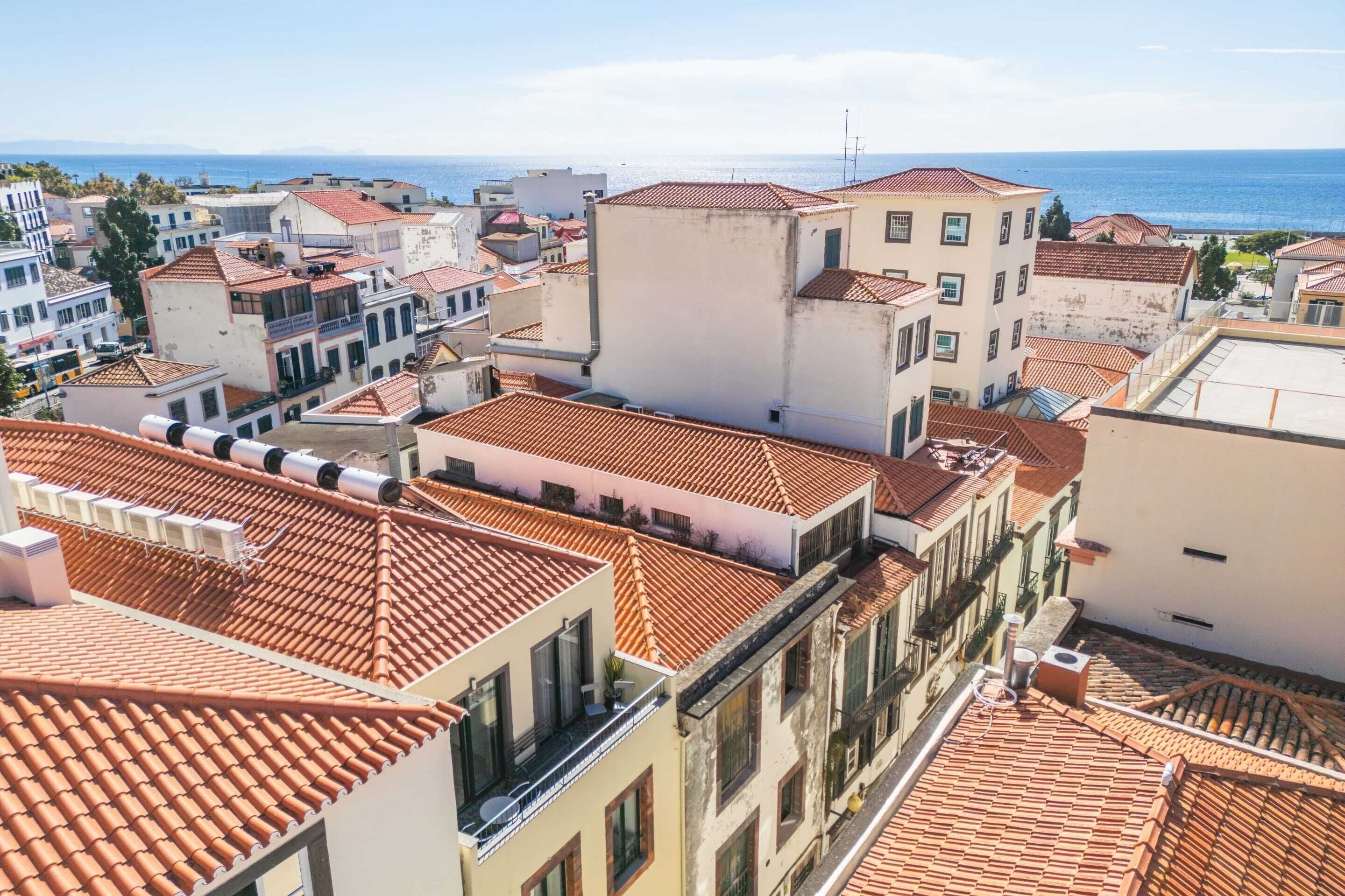 A coastal town with terracotta-tiled rooftops and white buildings, featuring a clear view of the sea.